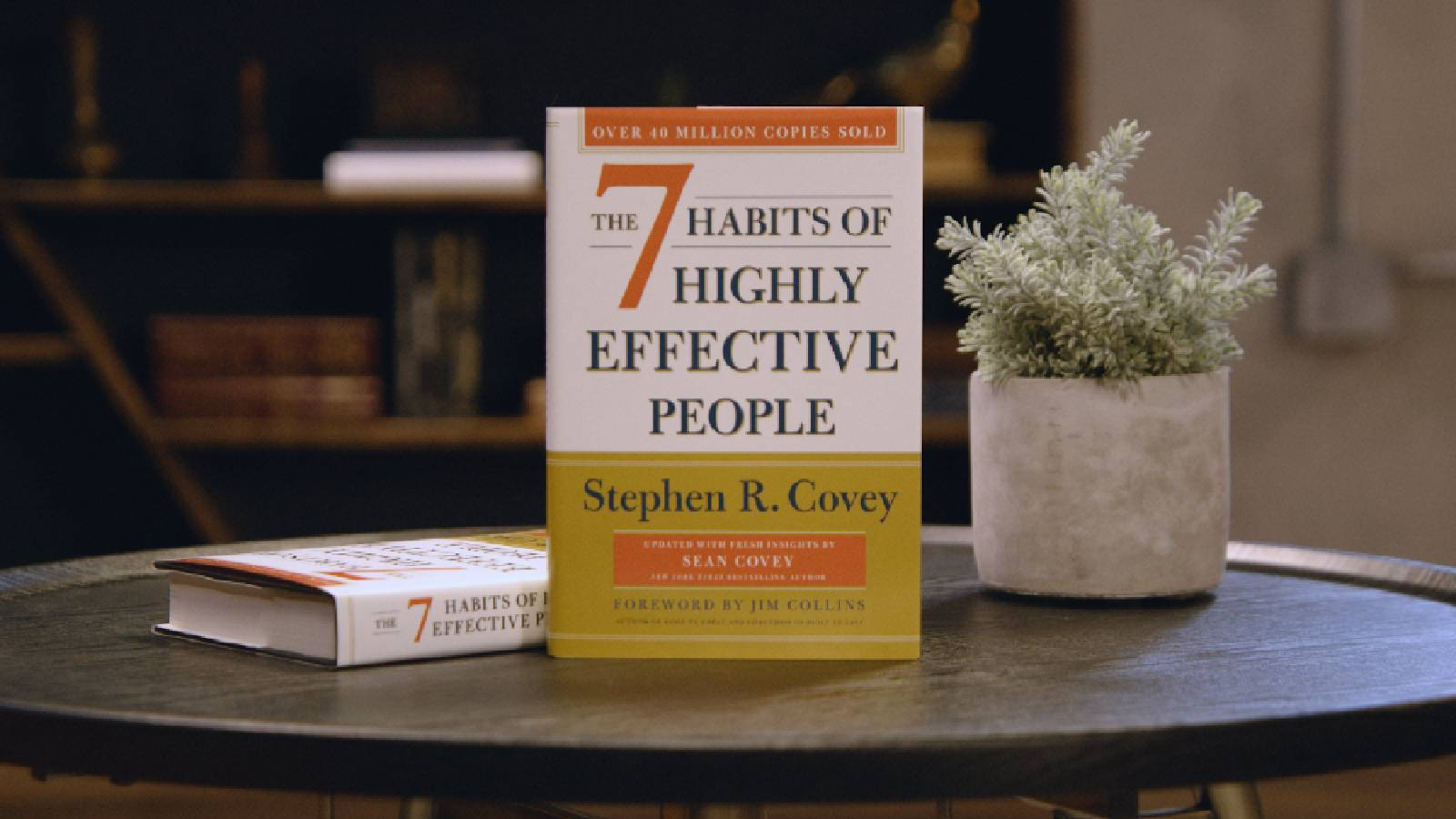 كتاب العادات السبع للأشخاص الفعالين  على طاولة تظهر بعض الورود البيضاء بجانبها كتاب العادات السبع للاشخاص الفعالين موضوع بشكل عامودي