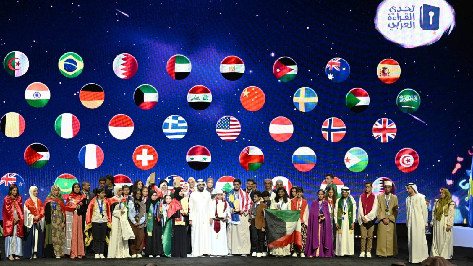 على خشبة المسرح يتم تكريم المشاركين في تحجي القراءة العربي و فوقهم بشكل افتراضي تظهر صور لاعلام الدول المشاركة 